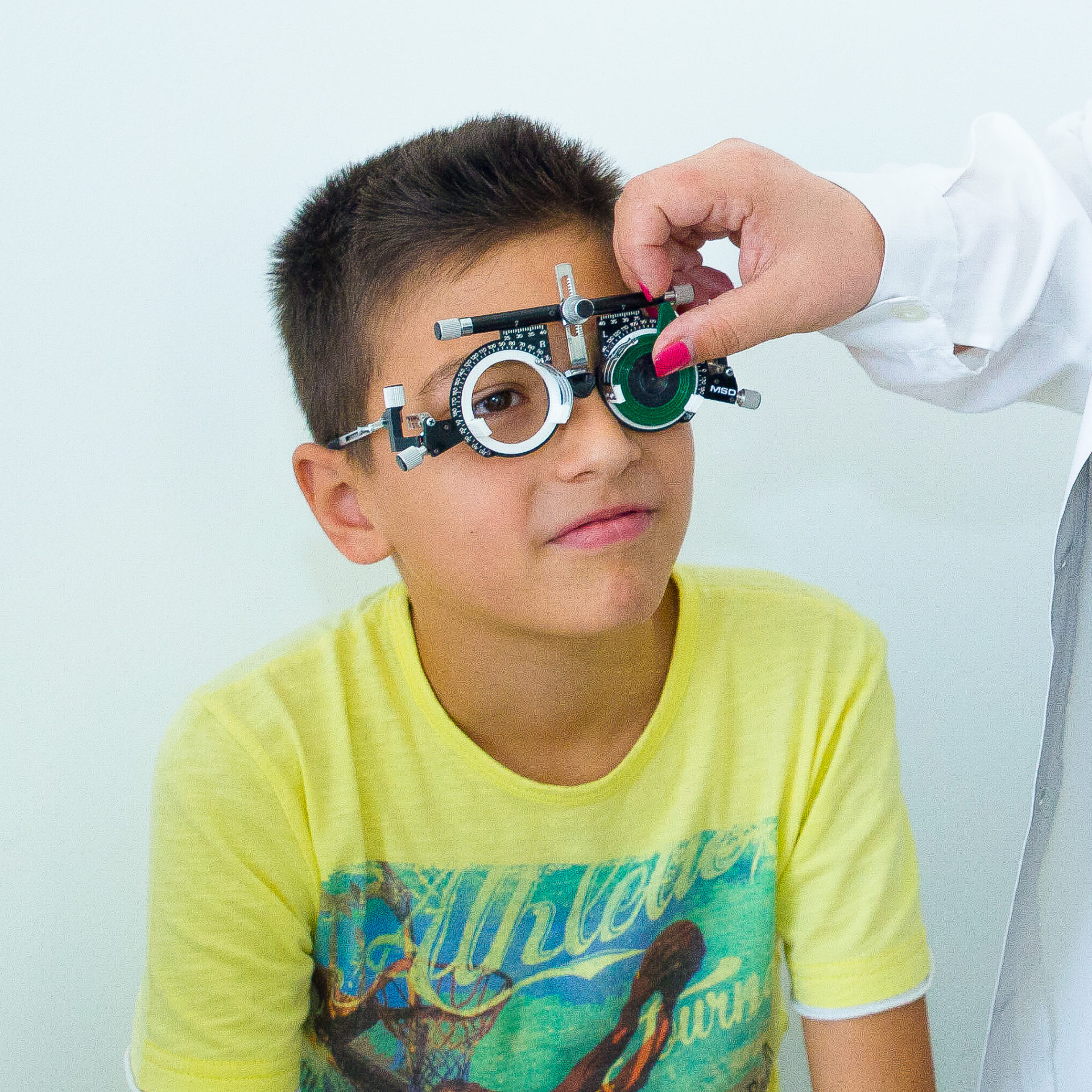 Il nostro oculista pediatrico sta eseguendo insieme alla sua assistente una visita con un bambino che lo guarda gli sorride